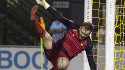 Soccer goalkeeper in maroon jersey diving horizontally to make a save, with yellow goal net visible behind.