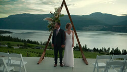 Bride and groom standing at wooden arch altar with lake and mountains in background.