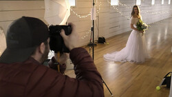 Photographer shooting a bridal portrait of a woman in a white wedding dress holding a bouquet in an indoor venue.