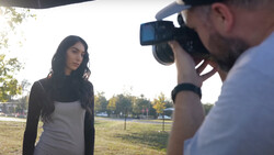 Photographer with DSLR camera photographing woman in casual clothing outdoors during golden hour.