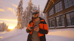 Man in bright orange jacket and dark cap standing in snowy landscape at golden hour.