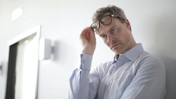 Man in light blue shirt and glasses looking at computer monitor with thoughtful expression.
