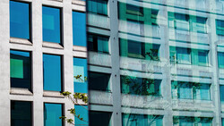 Modern residential building facade with contrasting blue and teal windows arranged in a grid pattern, separated by white concrete columns.