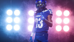Football player wearing number 23 in blue uniform posed against dramatic blue and pink stage lighting.