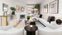 Contemporary living room with neutral furnishings, fireplace, and large windows overlooking urban street.
