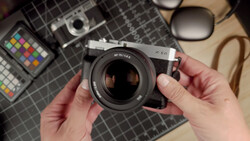 Photographer's hands holding a vintage rangefinder camera with fast lens over a flat lay of photography equipment.