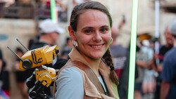 Woman holding yellow and black robot or mechanical device with antennae at an indoor event.