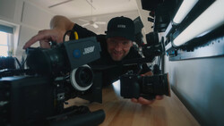 Filmmaker holding a cinema camera indoors, demonstrating equipment in a bright studio space.