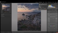 Coastal landscape at sunset with rocky cliffs, calm sea, and distant headland under dramatic clouds.