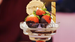 Chocolate-dipped strawberries in a clear glass bowl with a wafer cookie, shot with selective focus and warm studio lighting.