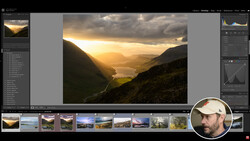 Mountain valley landscape with golden sunset light breaking through clouds over a lake and forested slopes.