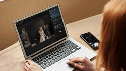 Photographer editing portrait images on laptop with smartphone nearby at wooden desk.
