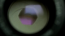 Close-up view through a camera lens showing a purple and blue aperture opening with light refraction.