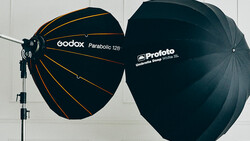 Two large parabolic umbrellas mounted on a stand: a Godox Parabolic 128 with gold interior and black exterior, and a Profoto umbrella with black exterior.