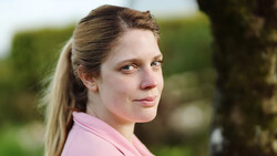 Woman in pink shirt looking over shoulder with soft natural outdoor lighting.