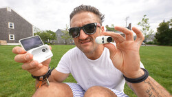 Man holding two compact cameras outdoors, displaying them toward the camera.