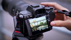 Videographer holding a mirrorless camera with an external monitor displaying a live feed of an interior scene.