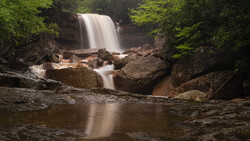 Waterfall cascading over rocky ledge surrounded by dense green forest foliage.