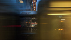 Motion-blurred subway train passing in front of historic theater marquee at dusk.