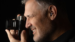 Male photographer holding binoculars-style camera to eyes against black background.