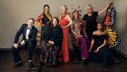 Group portrait of eight people in colorful formal and semi-formal attire posed against a neutral background.