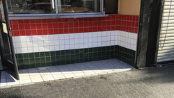 Storefront entrance with red, white, and green horizontal striped tile design on the recessed door area.