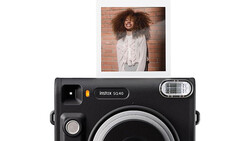 Instax SQ40 instant camera with sample portrait photo above showing smiling person against brick wall.
