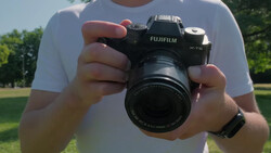 Photographer holding a Fujifilm X-T5 mirrorless camera with attached lens outdoors.