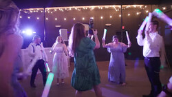 Wedding guests dancing under purple and warm string lights at an indoor reception venue.