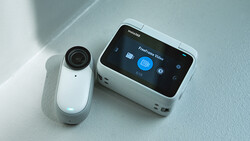 White action camera and portable gimbal stabilizer displayed on a light gray surface.