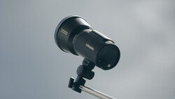 Studio flash or monolight mounted on a light stand against overcast sky.