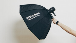 Photographer holding a Profoto octabox softbox with wooden handle against a neutral background.