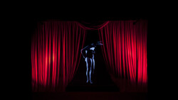 Silhouetted figure standing on stage between dramatic red velvet curtains lit from behind.