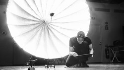 Photographer adjusting a large parabolic softbox reflector in a studio setting.