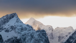 Snow-covered mountain peaks silhouetted against a golden sunrise sky with dramatic cloud layers.