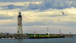 Historic stone lighthouse with multiple structures on a breakwater under dramatic cloudy skies.