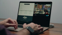 Hands using a laptop displaying split screens with a streaming interface and game footage.