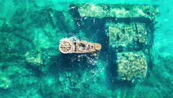 Aerial view of a shipwreck on shallow seafloor with a measurement scale showing the vessel's dimensions.