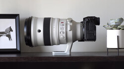 White telephoto lens mounted on black camera body, displayed horizontally on wooden shelf.