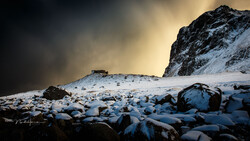 Snow-covered boulders scattered across a frozen landscape beneath a dramatic mountain peak.