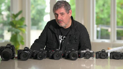 Photographer standing behind nine Nikon DSLR cameras arranged in a line on a white table.