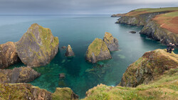 Moss-covered sea stacks surrounded by turquoise water beneath coastal cliffs.