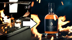 Bottle of Oliveum spirits positioned next to a dramatic studio lighting setup with flames and professional equipment.