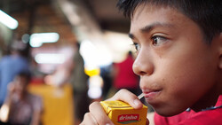Young person in red shirt holding a yellow beverage box in a crowded indoor space.