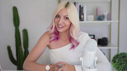 Woman with platinum blonde and pink ombre hair smiling at camera in bright studio setting.