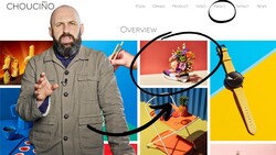 Man in tan jacket gestures while speaking, with colorful product photography examples displayed behind him.