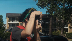 Photographer holding a DSLR camera up to their face while looking through the viewfinder outdoors.
