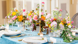 Elegant table setting with multiple colorful flower arrangements and tall taper candles.