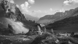 Alpine valley framed by steep rocky cliffs and forested slopes under cloudy sky.