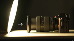 Camera lens and mirrorless camera body illuminated by bright directional studio lighting with an arrow pointing left.